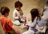 Three children sit on the floor, joyfully playing with various stuffed animals around them.