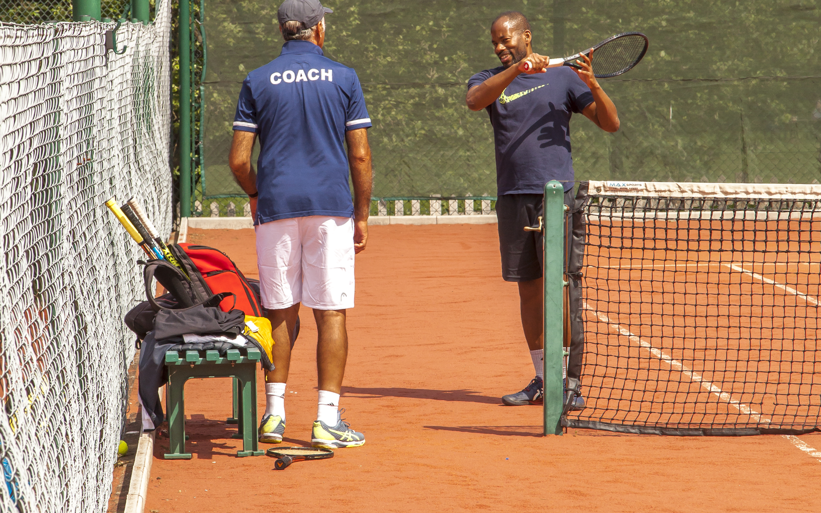 Two men stand talking on a clay tennis court
