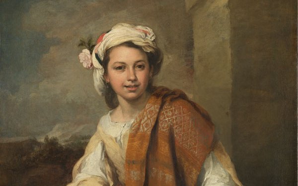 A girl in a flowing dress draped with a red patterned scarf in which she holds some flowers. On her head in a turban also with flowers in. She sits on a ledge and in the background is a landscape with large sky.