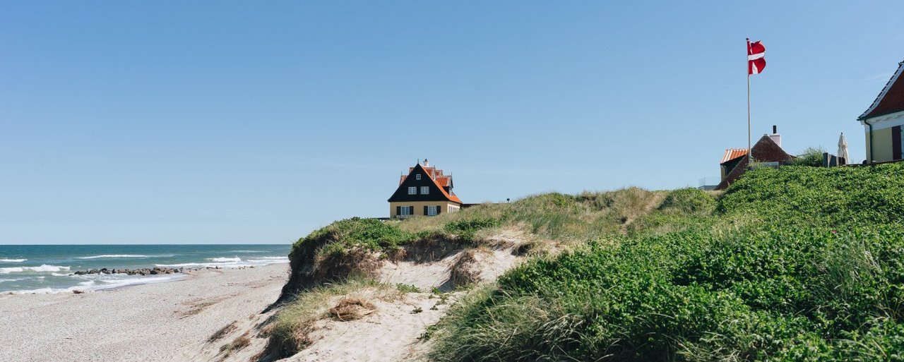 A beach with high dunes and a red house