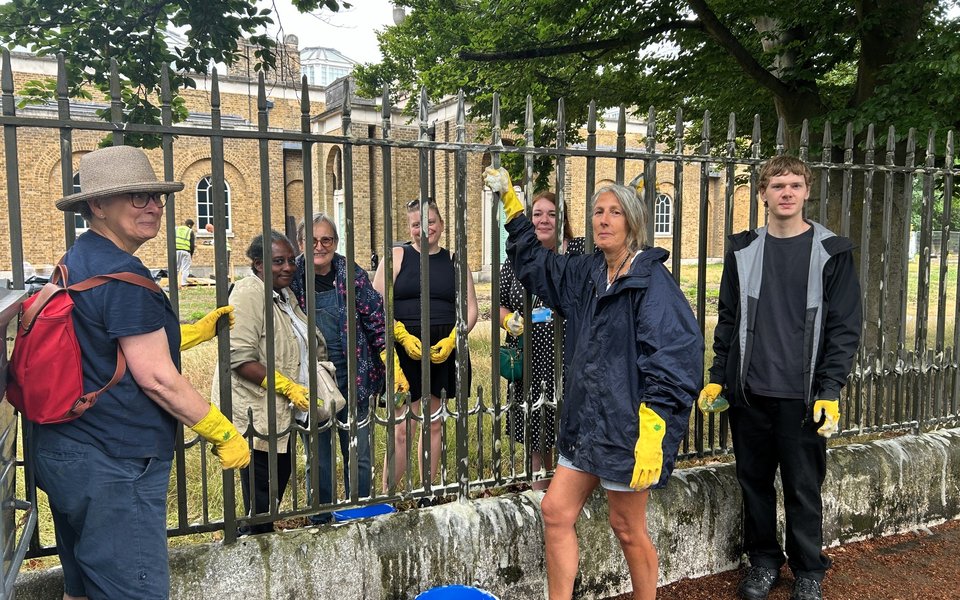 A group of volunteers stand either side of railings cleaning them.