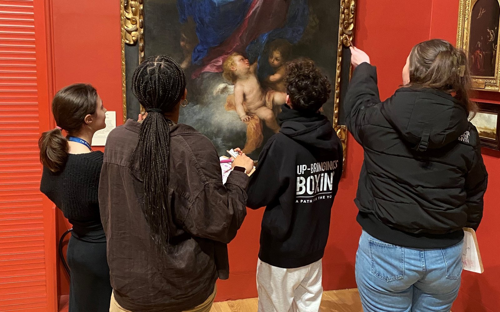 Small group of young people gathered around a gold framed painting.