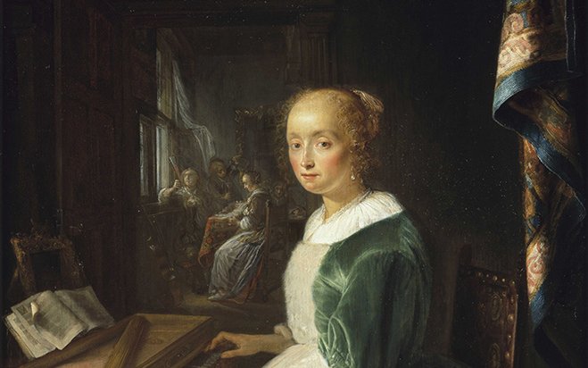 A young woman sat at a virginal in a green dress in an elaborate room