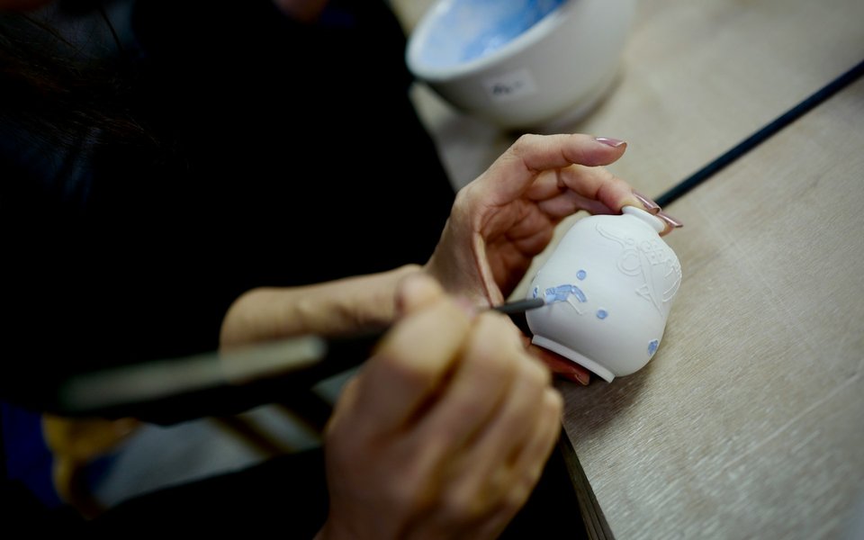 A person painting a bud shaped vase with a small brush - can only see hands