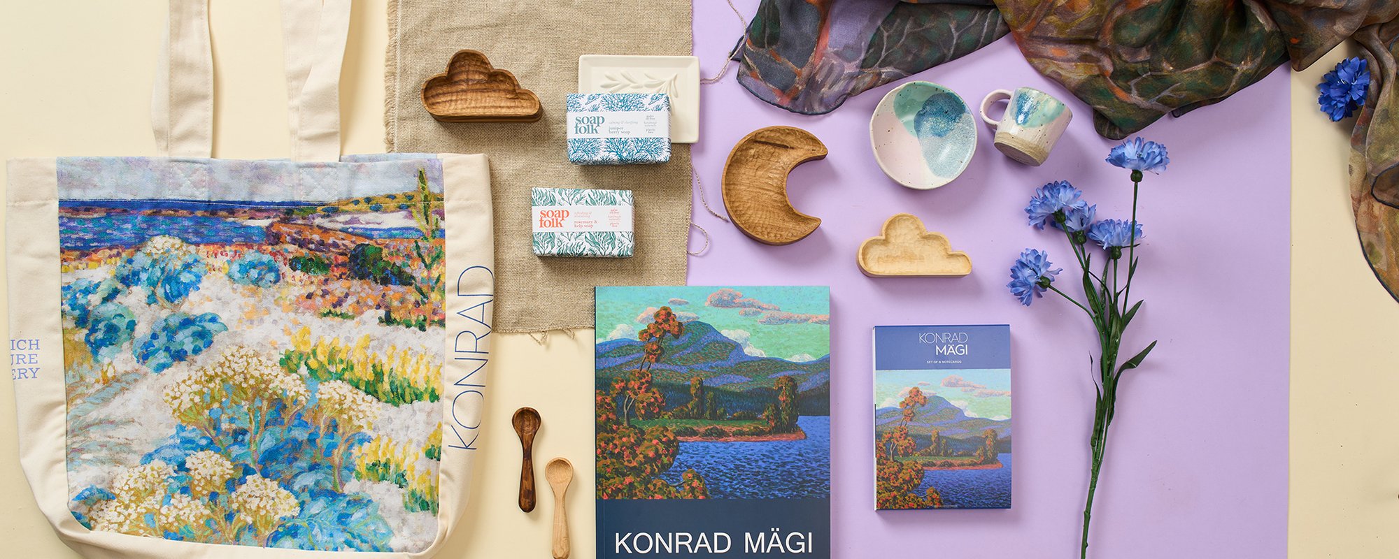 An assortment of merchandise for the Konrad Magi exhibition including a tote bag, ceramics, candles, a scarf and books.
